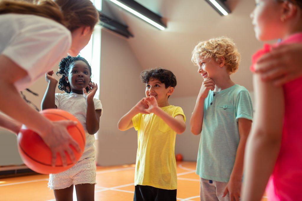 kinderen staan voor een gymdocent die een basketbal in de hand heeft